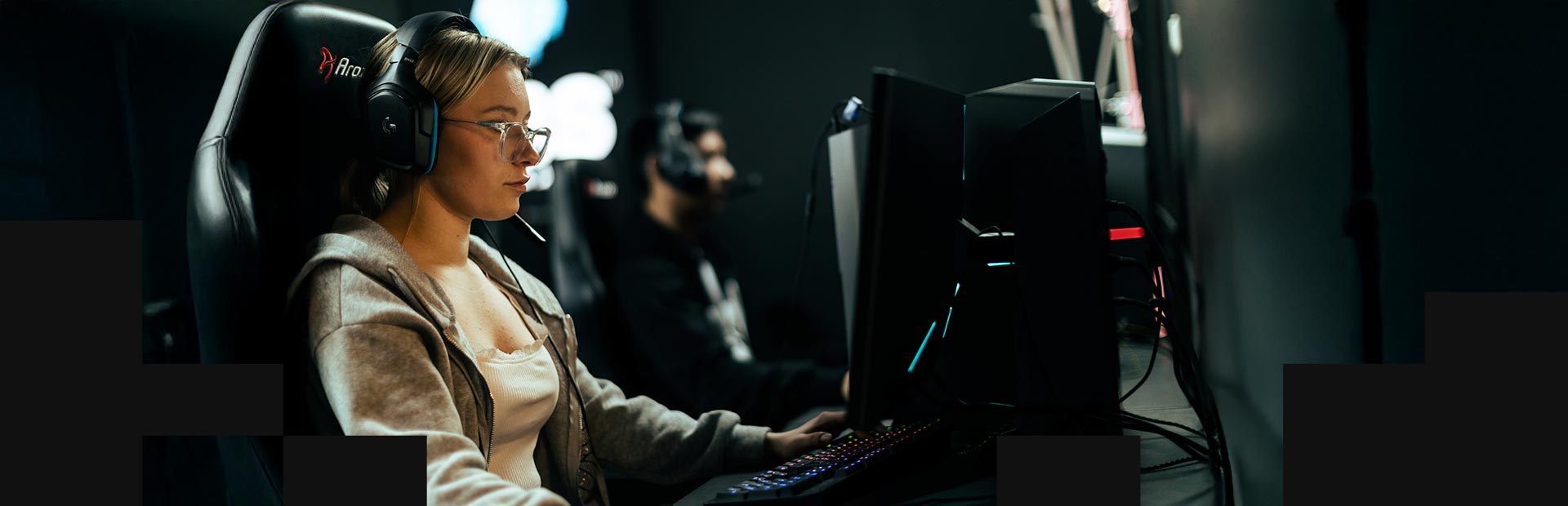 En tjej spelar e-sport vid dator i mörkt rum med headset och fokus på skärmen.